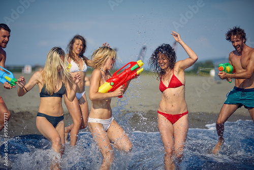 Happy people with water guns have fun on the beach