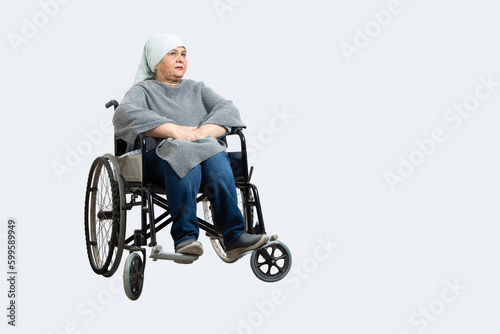 Senior indian woman cancer patient sitting on a wheelchair undergoing course of chemotherapy isolated over white background. Healthcare concept. Copy space.