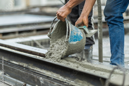 A male worker in a precast wall manufacturing factory (Precast) is pouring cement in a prepared mold to form a wall.