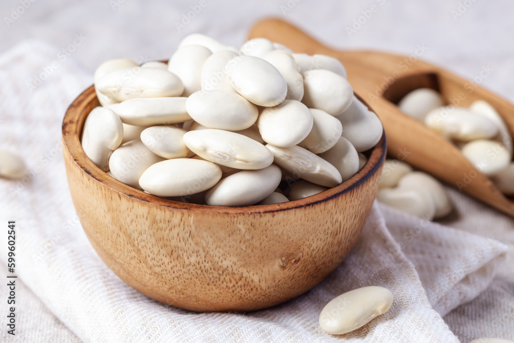 Raw white beans in wooden bowl with scoop on linen tablecloth Raw white beans in wooden bowl with scoop on linen tablecloth