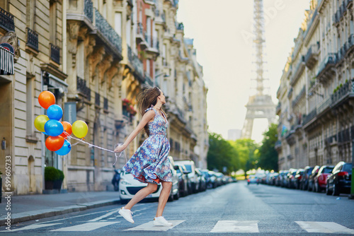 Beautiful young girl with colorful balloons running across the street in Paris