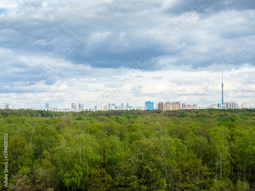 gray rainy clouds over green forest and city on horizon on spring day