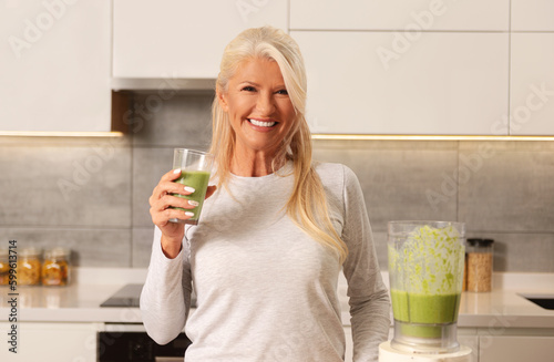 Beautiful, older woman drinking a healthy green - fruit and vegetable smoothie.