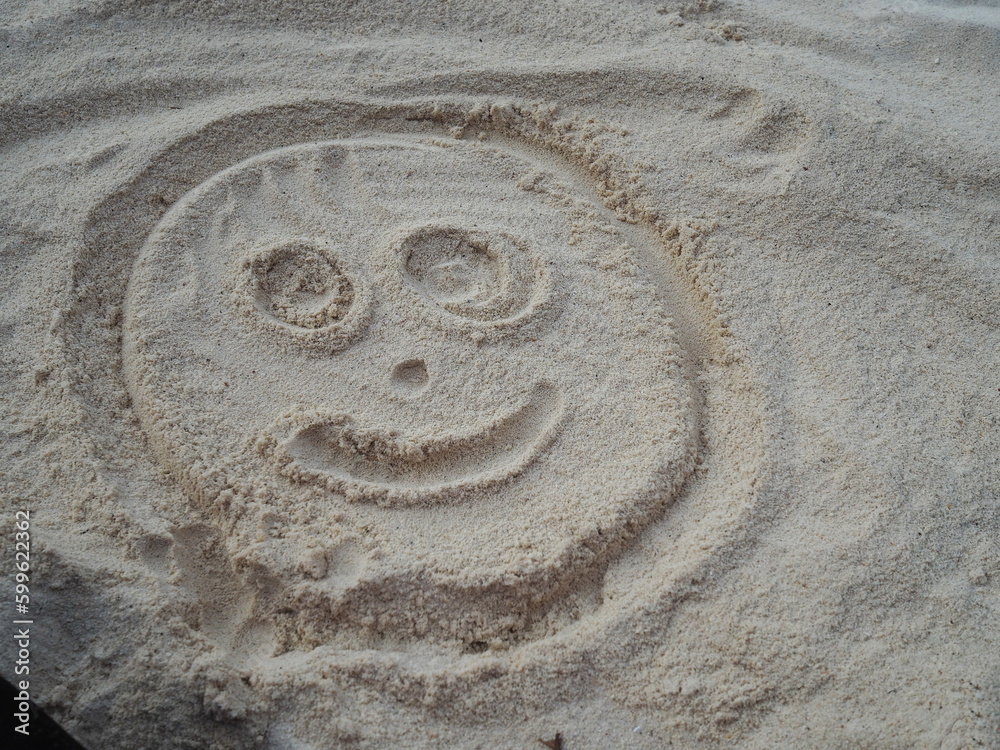 Draw a circle. Add a smiling, eye, nose and mouth in sand. People like to draw on sand in various shapes. While going on beach vacation. The smiling face of doll shows that the painter is happy.
