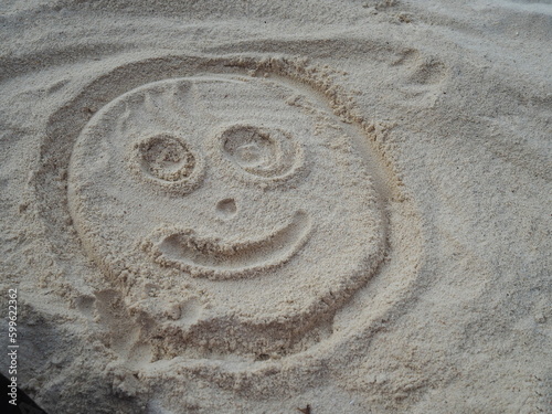 Draw a circle. Add a smiling, eye, nose and mouth in sand. People like to draw on sand in various shapes. While going on beach vacation. The smiling face of doll shows that the painter is happy. 