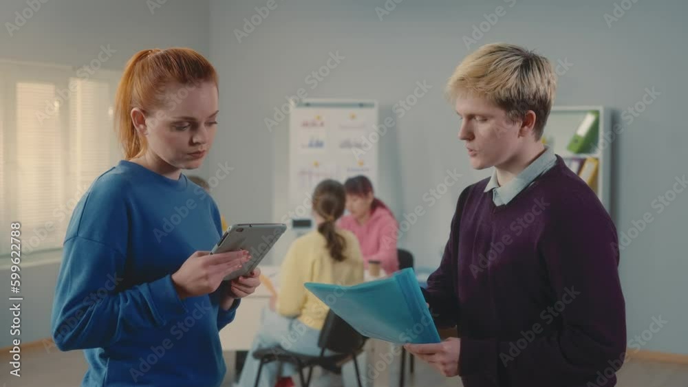 Young man and woman are discussing a new business project and checking the data in a digital tablet and a document. Group of young managers working together in a modern office. Young man and woman are discussing a new business project and checking the data in a digital tablet and a document. Group of young managers working together in a modern office.
