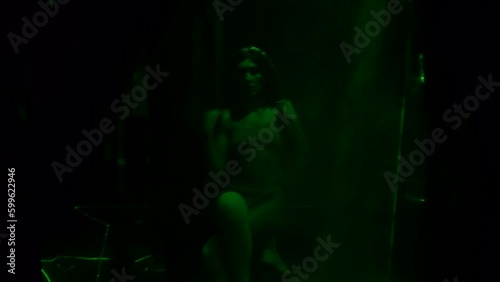 enigmatic sexy woman in lingerie moving seductively sitting in dark room with green laser rays
