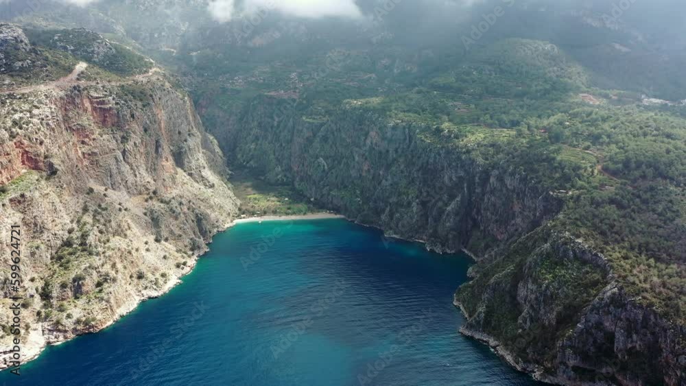 The Butterfly Valley (Kelebekler vadisi) in the city of Oludeniz, Turkey. A picturesque steep slope, a canyon, a beautiful wild beach surrounded by mountains. Aerial view. The Butterfly Valley (Kelebekler vadisi) in the city of Oludeniz, Turkey. A picturesque steep slope, a canyon, a beautiful wild beach surrounded by mountains. Aerial view.