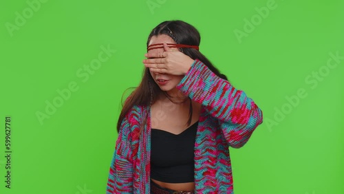 Nosy curious young woman closing eyes with hand and spying through fingers, hiding behind hand fingers, peeping gesture exploring way seeking something in distance. Girl on green chroma key background