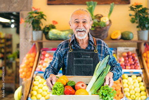 Senior greengrocer working at the market holding a box containing fresh fruits and vegetables - Food retail concept photo