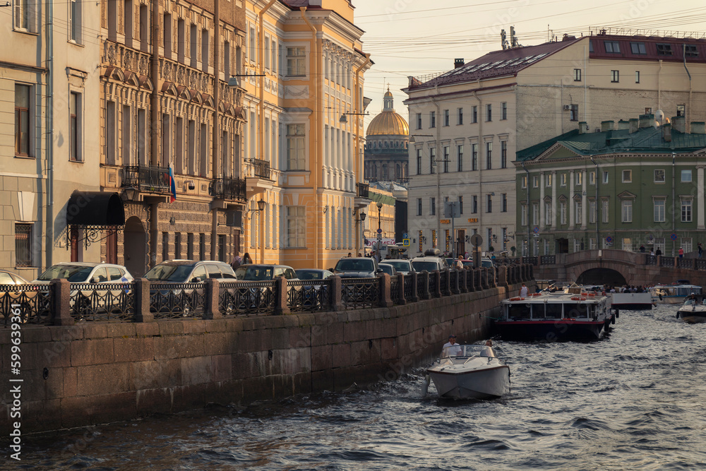 Evening view of St. Petersburg street. Boats on a river surface against cars on an embankment and a Saint Petersburg cityscape by summer day