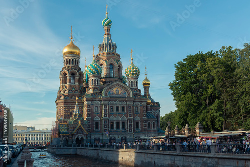 A low angle shot of a river and people on an embankment in front of the Church of the Savior on Spilled Blood against a cupola by summer day