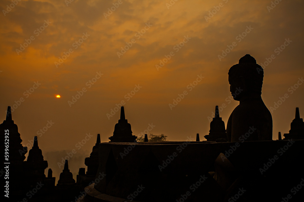 Silhouettes of Buddha statues and stupas in the Borobudur Temple complex at sunrise. Borobudur Temple is the largest Buddhist temple in the world, located in Magelang, Yogyakarta, Indonesia.