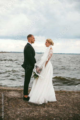 Groom and bride standing at the sea shore against the wind
