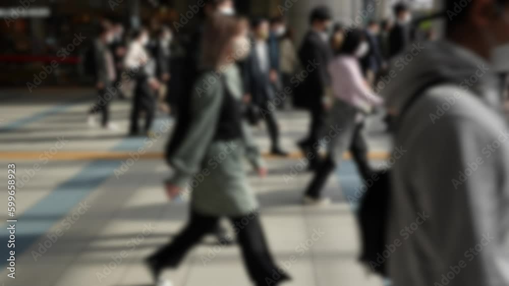 Blurred defocused view of commuters flooding out of the metro station in Japan, all headed in the same direction towards their offices. A bustling crowd of people march down the busy street Blurred defocused view of commuters flooding out of the metro station in Japan, all headed in the same direction towards their offices. A bustling crowd of people march down the busy street