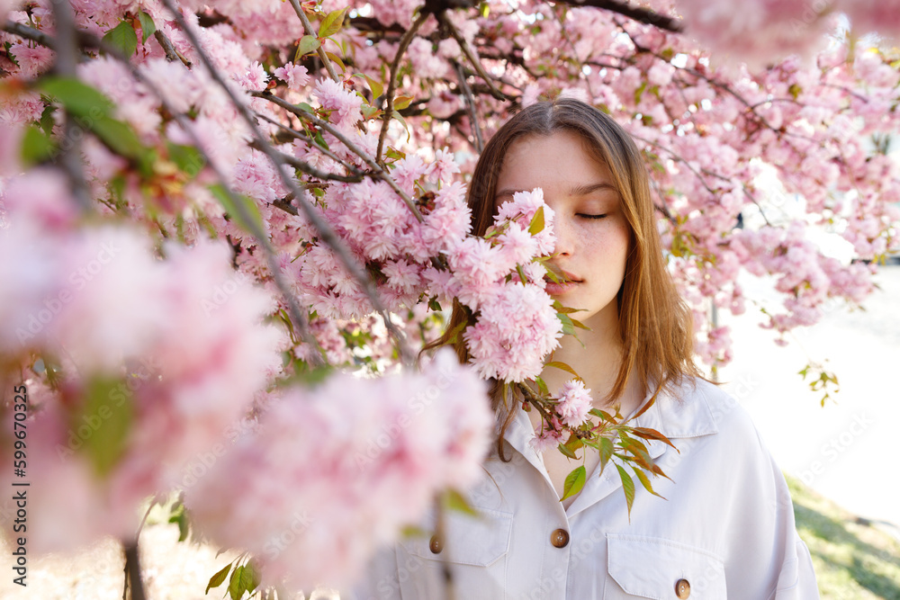 Sensual Beautiful Girl With Brown Hair Covering Half of Face With Branches of Blooming Sakura Tree. Woman Standing in the Park. Seasonal Flowering and Femininity Concept. Face Portrait Sensual Beautiful Girl With Brown Hair Covering Half of Face With Branches of Blooming Sakura Tree. Woman Standing in the Park. Seasonal Flowering and Femininity Concept. Face Portrait