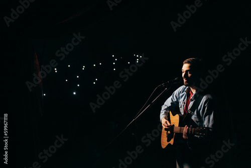 The singer plays an acoustic guitar and sings at a concert © andrew_shots
