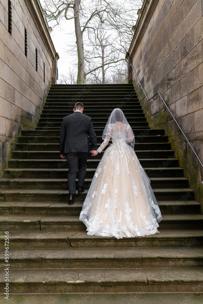 Fototapeta premium .The bride and groom are walking along the stone steps of an ancient building, a palace. Rear view, from the back. The bride is wearing a beautiful long dress.