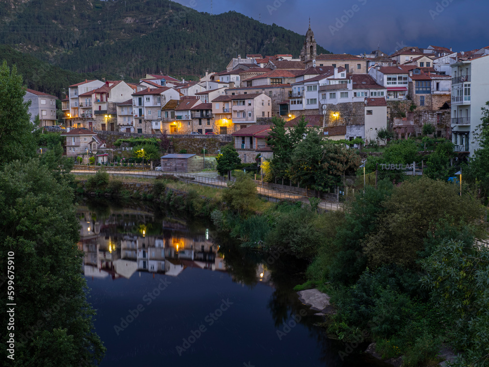 Night view of the town of Ribadavia in Orense, reflected with the lights in the Avia river, with the bell tower and white houses, in the background the mountain in summer of 2021 Spain