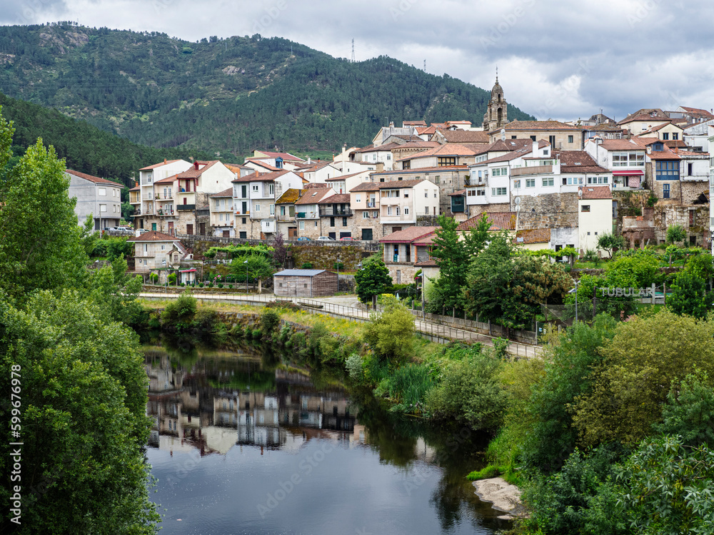View of the town of Ribadavia in Orense, reflected in the Avia river, on a cloudy day, with the bell tower and white houses, in the background the mountain in summer of 2021 Spain