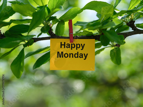 A yellow paper note with the phrase Happy Monday on it attached to a tree branch with a clothes pin