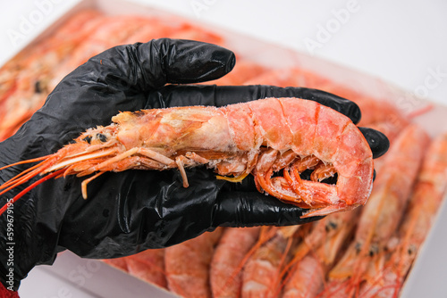 In the hand of the cook in a black glove lies a large frozen langoustine. Close-up. photo