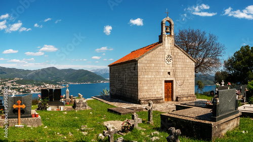 Orthodox church with old stone graves in green grass front view with sea and mountains at background