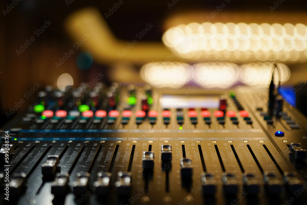 Faders pushed up on audio mixer console with LED buttons in bokeh in well lit ballroom.. Lights are blurred for effect. Faders pushed up on audio mixer console with LED buttons in bokeh in well lit ballroom.. Lights are blurred for effect.