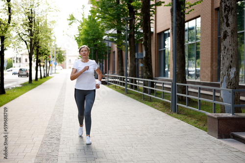 Portrait of the Posotive Mature Lady Running and Wearing Eeadphones in the Street. Sport and Healthy Lifestyle Concept