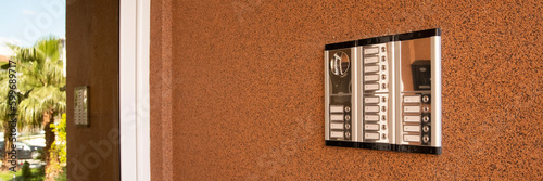 Entrance doorbell in multi-apartment building, with intercom device, on brown wall photo