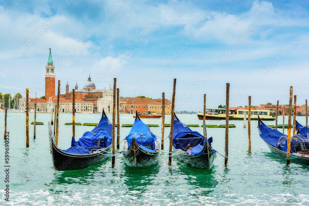 Gondolas moored by Saint Mark square with San Giorgio di Maggiore church in the background, Venice, Italy. Beautiful sky and green water