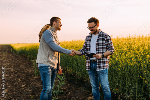 Two businessman standing in the oil rape field and shaking hands.