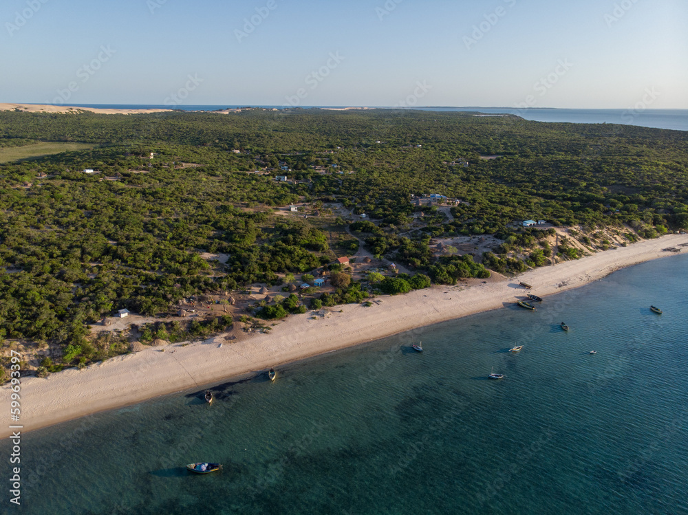 Luftaufnahme von einem Strand in Mosambik, Afrika, mit mehreren kleinen Fischerbooten auf dem Meer vor dem weiten Sandstrand mit Palmen