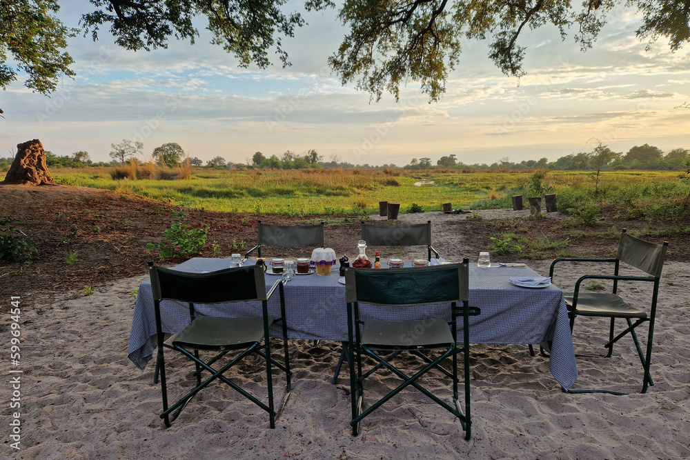 Ein gedeckter Tisch zum Abendbrot mit weißer Tischdecke unter freiem Himmel in einer Lodge im Okavango Delta, Afrika Ein gedeckter Tisch zum Abendbrot mit weißer Tischdecke unter freiem Himmel in einer Lodge im Okavango Delta, Afrika