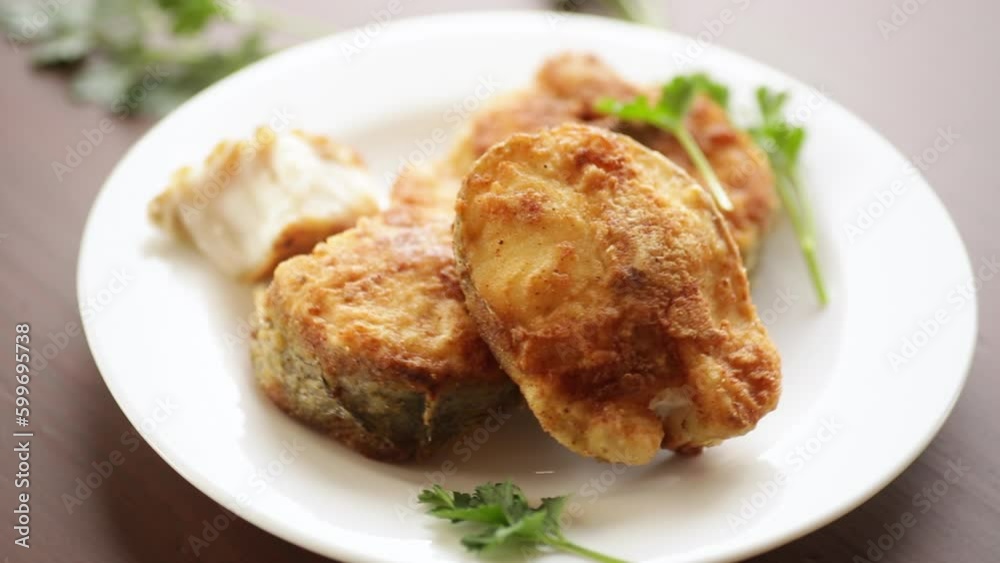 A piece of hake fish fried in a crispy crust, in a plate. A piece of hake fish fried in a crispy crust, in a plate.