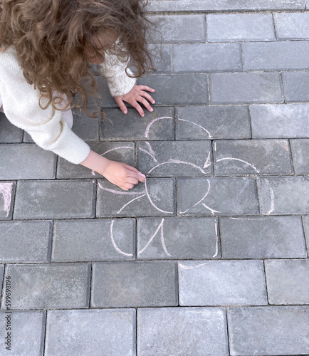 A little girl draws with chalk on the sidewalk