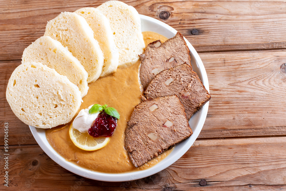 Plate of svickova na smetane, popular traditional Czech meat dish with sirloin steak prepared with vegetables, served with knedliky (dumplings), whipped cream and cranberry sauce on the table.