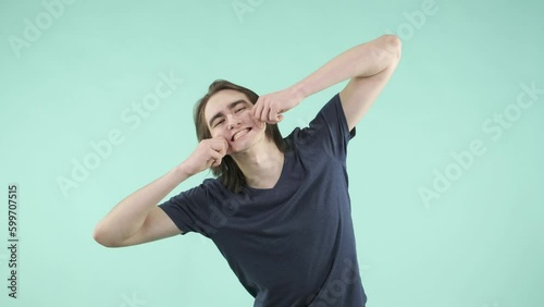 A young man with friendly manners and an emotional facial expression playfully interacts with the camera, dressed in a T-shirt and standing against an isolated background.