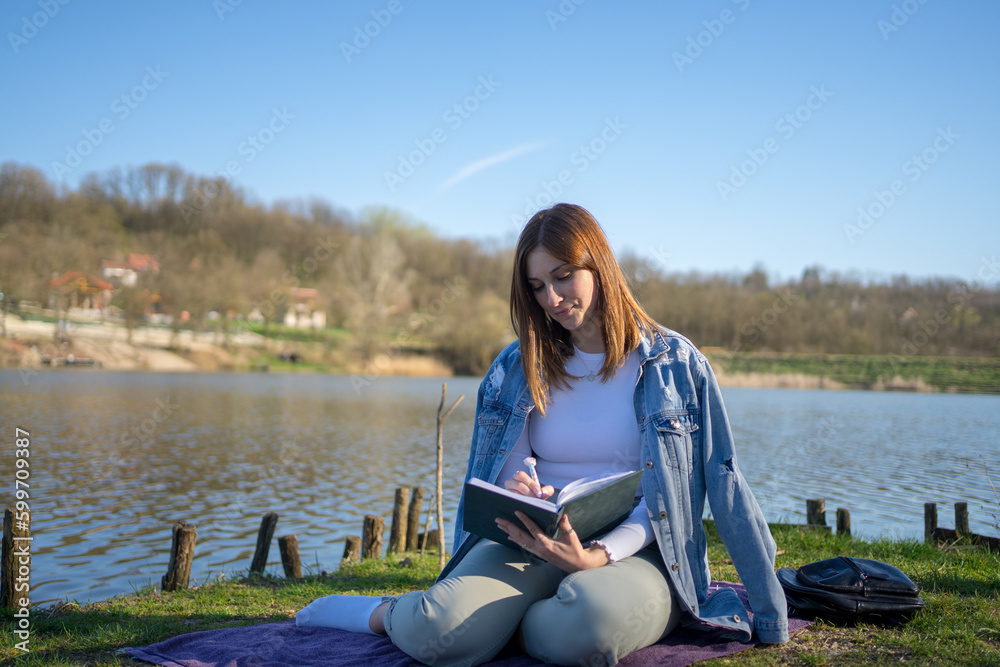 Woman at lakeside writing in a notebook. Nature concept. Self reflection.