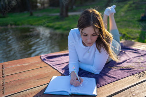 Woman at lakeside writing in a notebook. Nature concept. Self reflection.