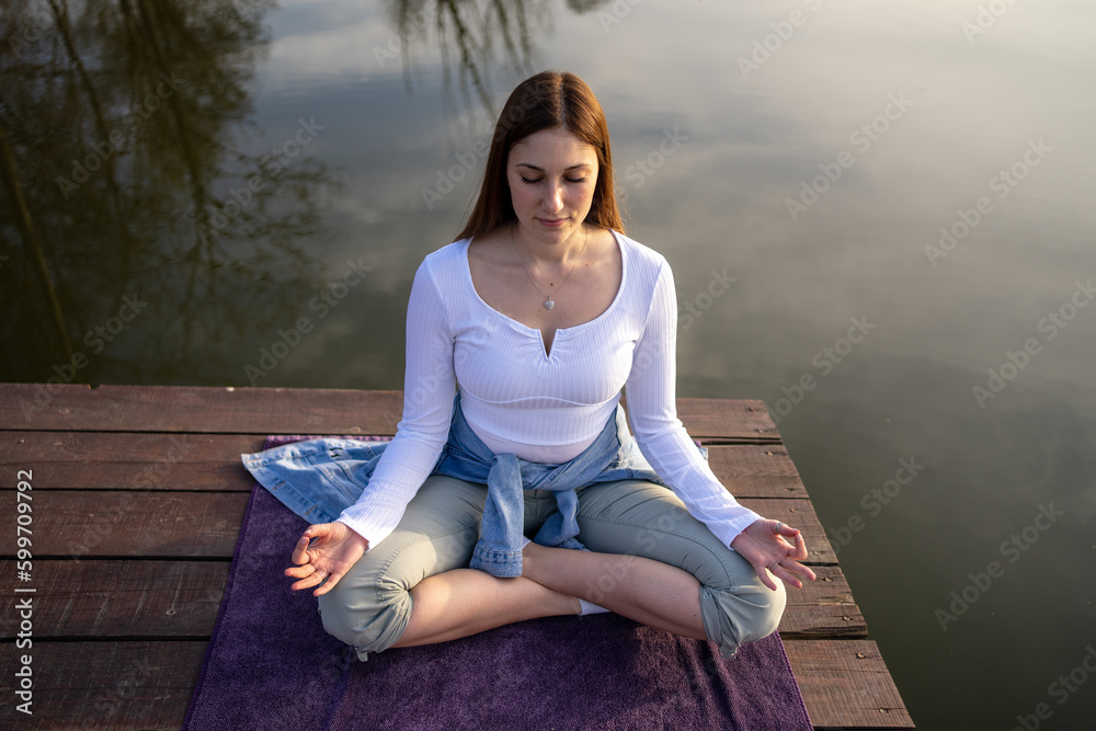 Woman relaxingly practicing meditation in nature by the lake. Nature background. Spiritual and emotional concept.