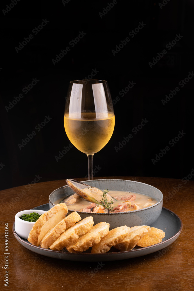 seafood soup with New Zealand mussels toast and green onions on wooden table portrait with glass of white wine