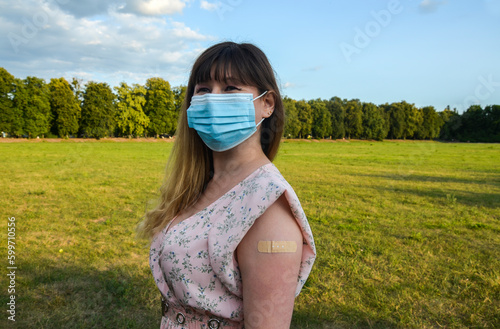 Attractive beautiful girl wearing blue protective mask shows a bandage applied after getting vaccination. Coronavirus covid-19 vaccine. Immunization program. 