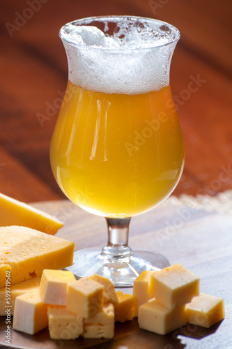 Glass of Belgian light blonde beer made in abbey and wooden board with variety of belgian cheeses photo