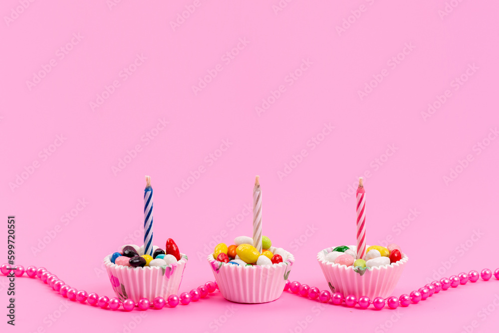 a front view colorful candies inside white paper packages with candle on the pink background sugar sweet confectionery a front view colorful candies inside white paper packages with candle on the pink background sugar sweet confectionery
