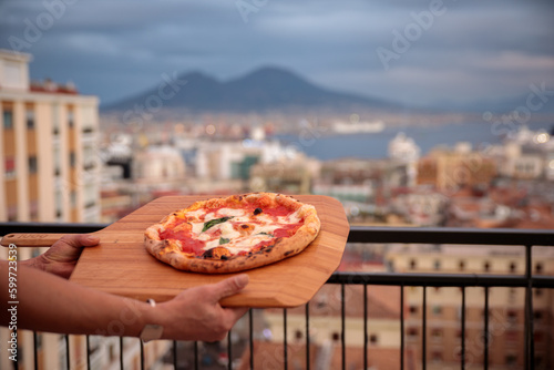 Pizza Napoletana offerta su un vassoio di legno con il Vesuvio e la città di Napoli alle spalle photo