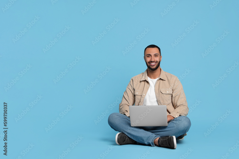 Smiling young man with laptop on light blue background, space for text