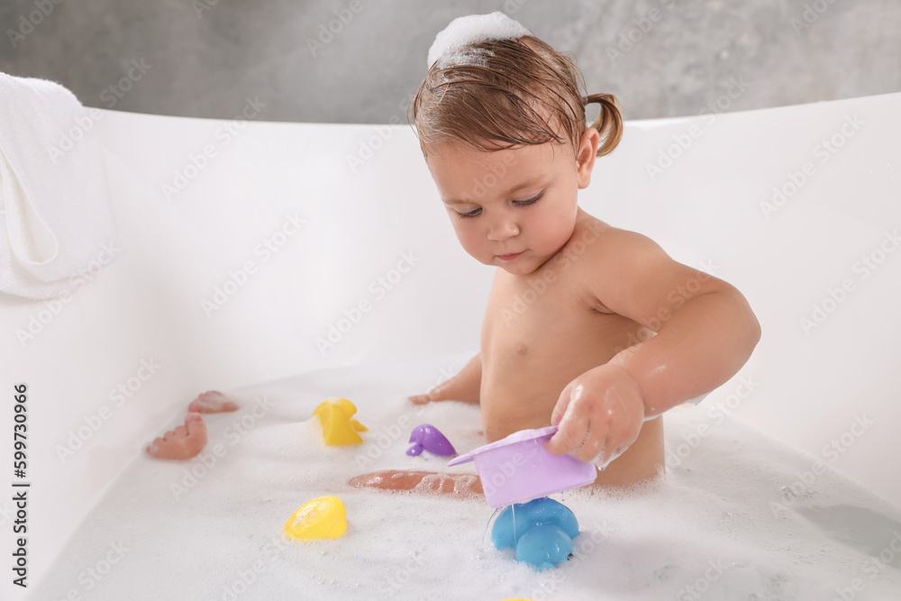 Cute little girl taking bubble bath with toys indoors Cute little girl taking bubble bath with toys indoors