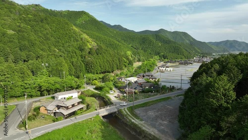 Kei truck drives by Japanese house and flooded rice fields in mountain landscape