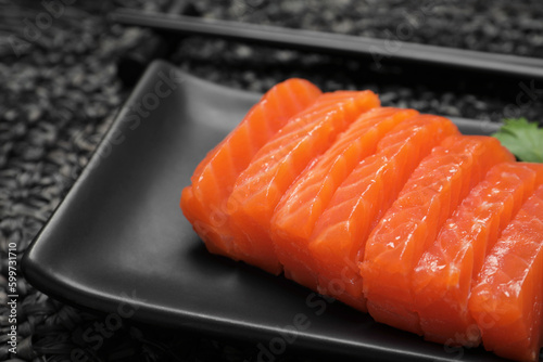 Plate of tasty salmon slices on black wicker mat, closeup. Delicious sashimi dish